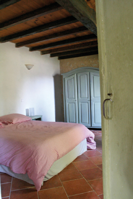 Terre cuite, plafond en poutres apparentes, murs de pierre enduits à la chaux, et meubles patinés, cette chambre forme un ensemble représentatif des options de décoration prises dans le cadre de réhabilitation.